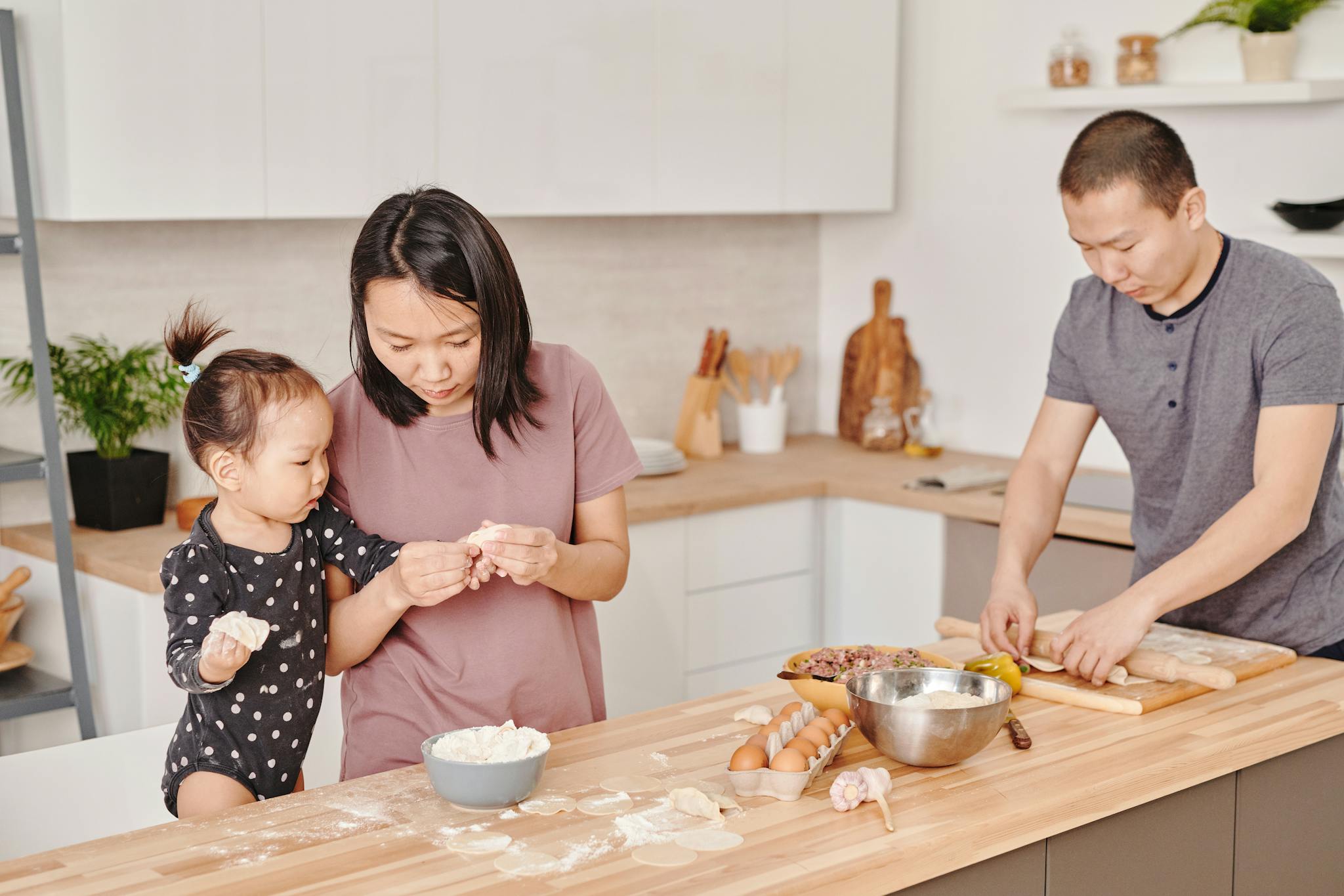 Asian family making dumplings together in a cozy kitchen. Parents teaching child food preparation.