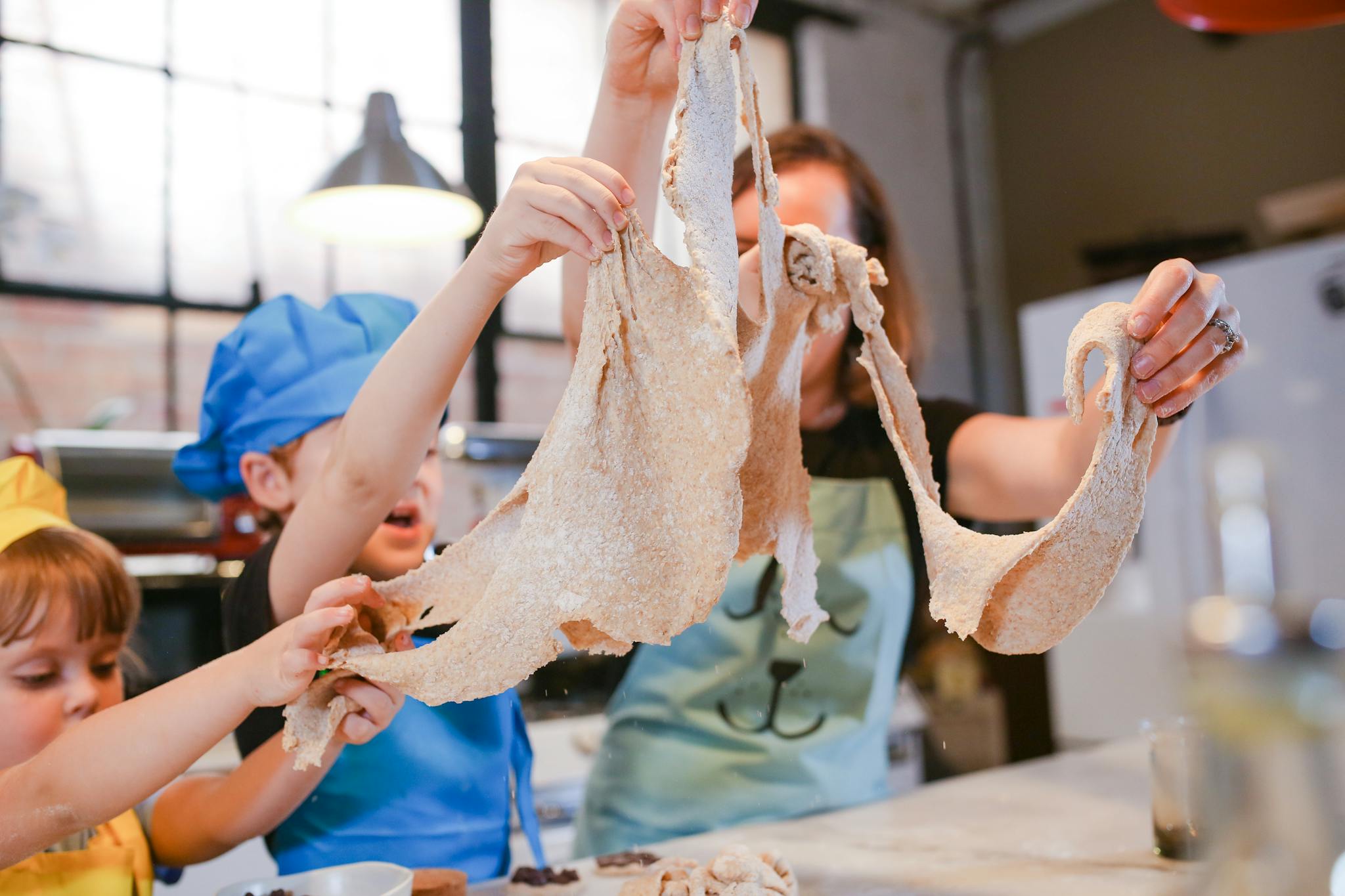 Happy children and adult making dough together in a vibrant kitchen setting.